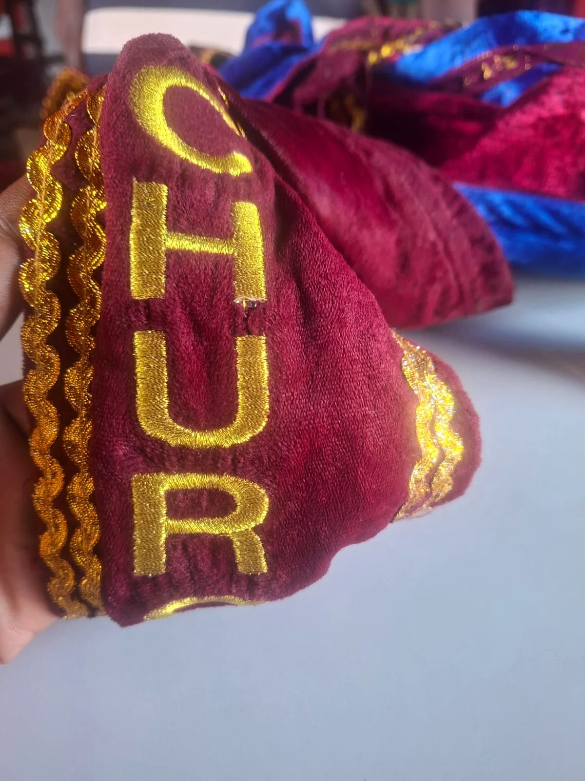 Metallic-gold lettering embroidered onto burgundy fabric.